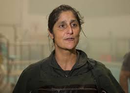 Sunita Williams wearing a training suit, looking slightly tired but focused, inside a spacecraft simulation facility.